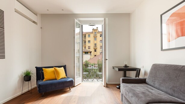 A modern living room with a sofa, a small table, and a view through an open door to a balcony. - GuestHost - Modern and comfortable apt - central station! (Milano)