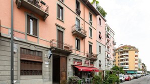 A multi-story building with a restaurant on the ground floor, featuring outdoor seating and a red awning. - GuestHost - Modern and comfortable apt - central station! (Milano)
