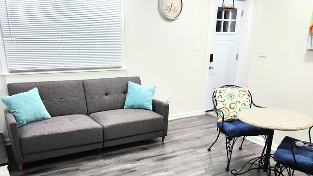 A modern living room with a grey sofa, two blue cushions, a round table with a woven top, and a patterned chair. - Modern Oasis near everything. (Nashville)