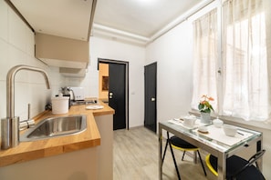 A compact kitchen with a sink, a small dining table, and a window with curtains.