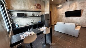 A modern kitchen with a dining area, a sofa, and a TV mounted on the wall. - Coco Live Suites (Playa del Carmen)