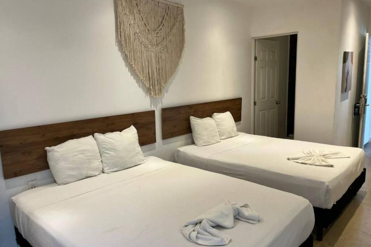 Two beds with white linens, a wooden headboard, and a macrame wall hanging.