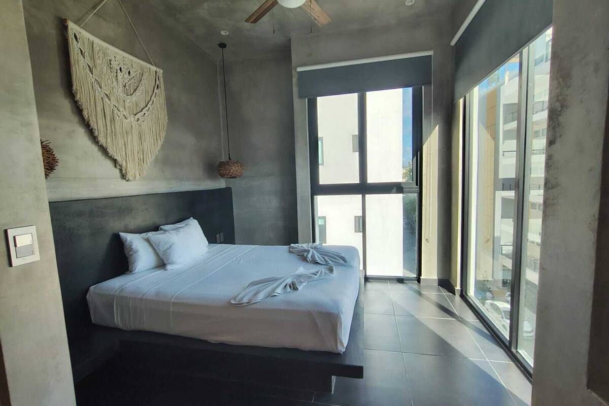 A modern bedroom with a bed, a ceiling fan, and a large window.