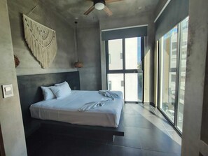 Un dormitorio moderno con una cama, un ventilador de techo y un ventanal grande.