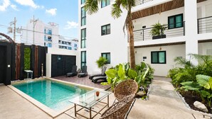 A modern building with a swimming pool, outdoor seating, and lush greenery. - Coco Live Suites (Playa del Carmen)