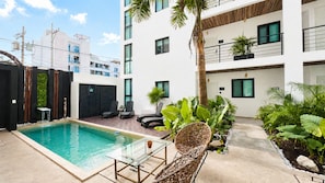 Un edificio moderno con piscina, mobiliario exterior y abundante vegetación.
