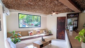 A modern interior with a sofa, a coffee table, a window with a view of greenery, and a reception desk. - Enigmatic Boutique Hotel (Cancun)