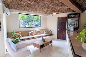 A modern interior with a sofa, a coffee table, a window with a view of greenery, and a reception desk. - Enigmatic Boutique Hotel (Cancun)