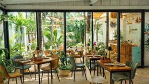 Un restaurant doté de grandes fenêtres, d’une terrasse et de plantes tropicales.