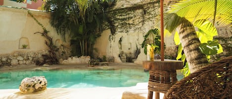 A pool area with a stone wall, tropical plants, and a wicker chair.