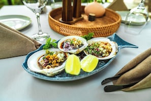 Un plato de mariscos sobre una fuente azul, con gajos de lima, colocado sobre una mesa con una cesta tejida y un florero de vidrio.