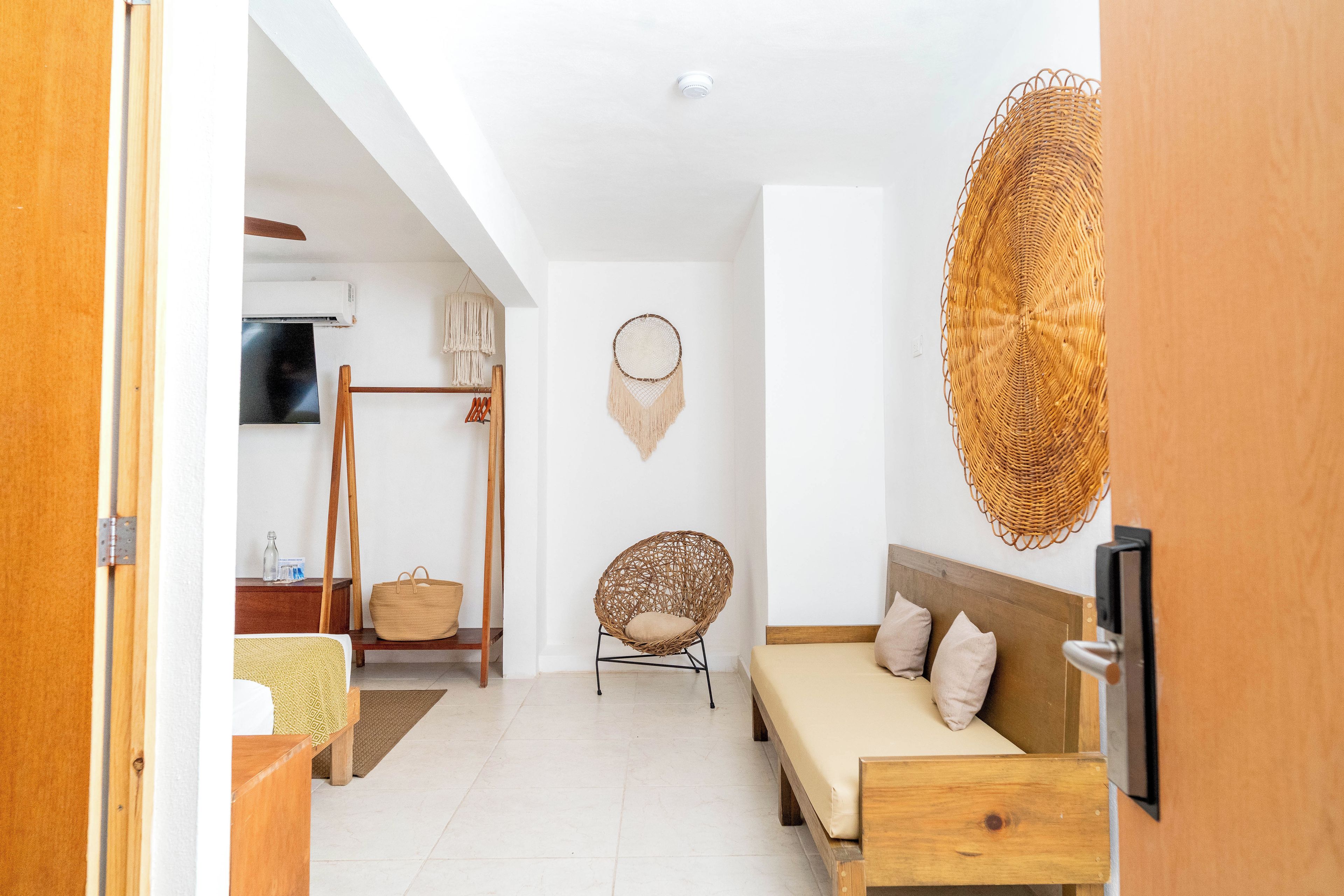 A room with a bed, a chair, a wall-mounted TV, and a woven wall hanging.