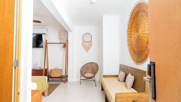 A room with a bed, a chair, a wall-mounted TV, and a woven wall hanging.