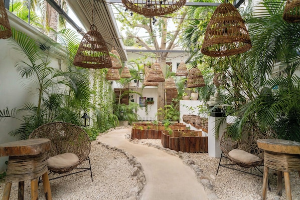 Un jardín tropical con mobiliario de mimbre, un sendero de grava y cestas colgantes.