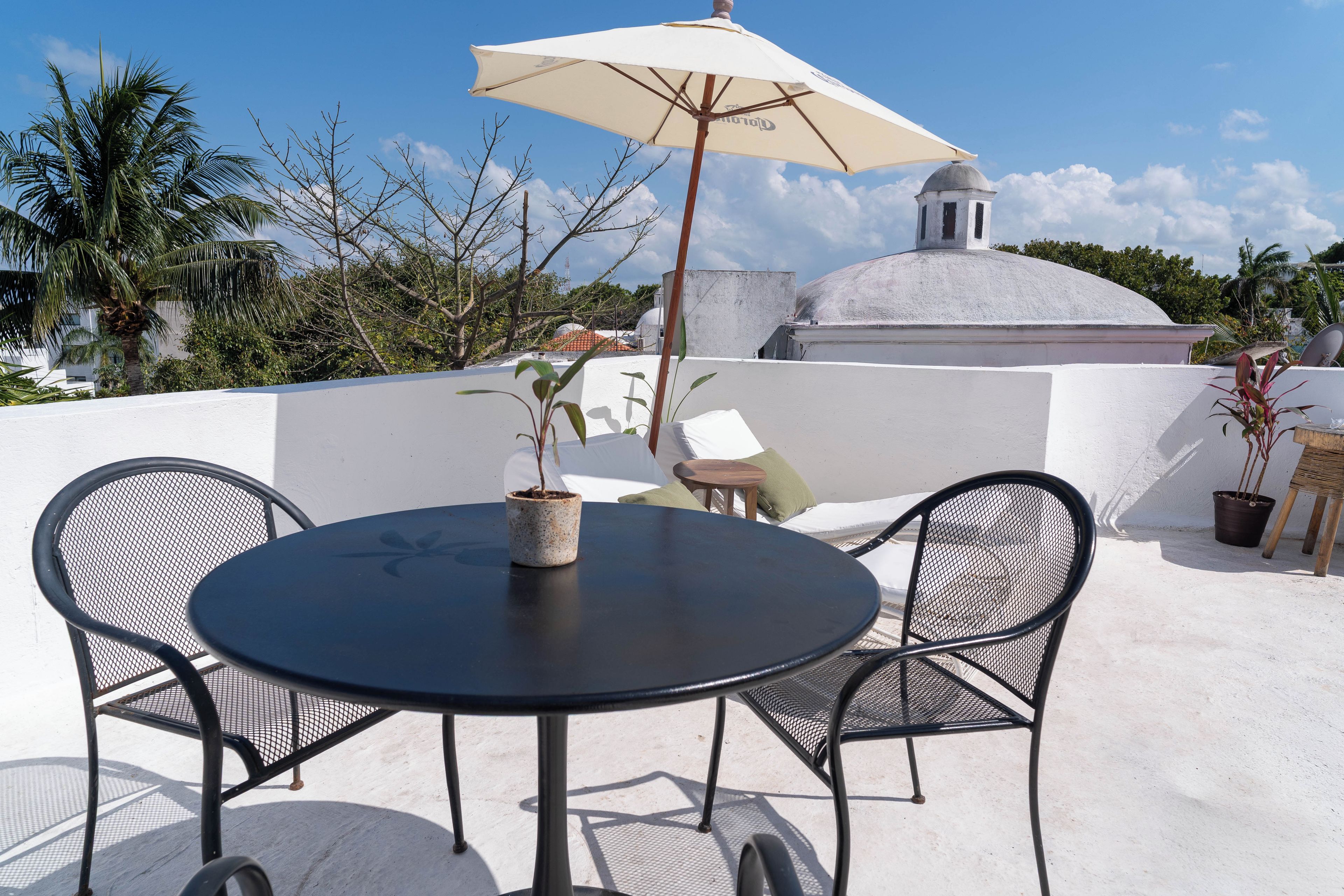 An outdoor seating area with a round table, two chairs, a potted plant, and a large umbrella.
