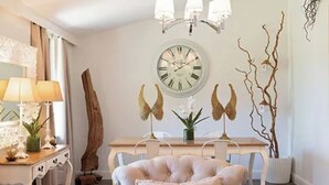 Un comedor con un reloj de pared redondo, una escultura de madera y una silla tapizada blanca.