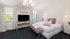 Un dormitorio con una cama grande, un televisor sobre un mueble bajo, un banco y una mesita de noche con lámpara.