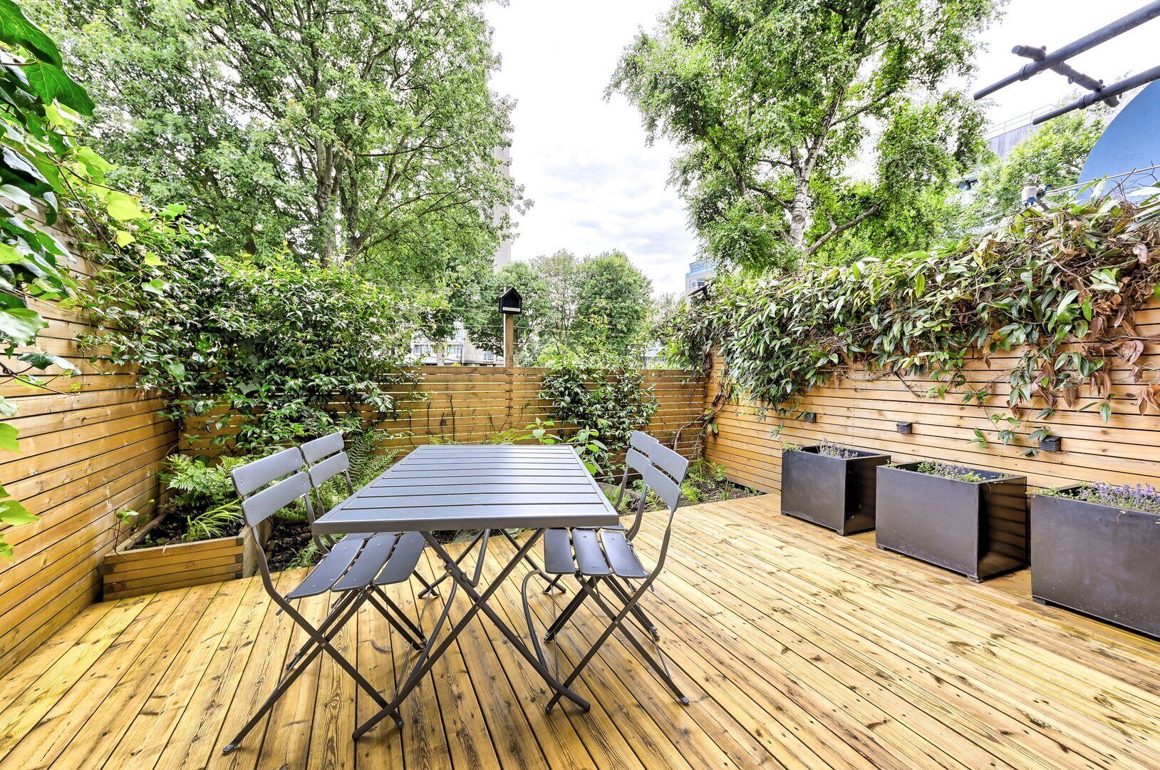 An outdoor patio with a wooden deck, a metal table, and chairs.