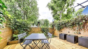 Un patio al aire libre con terraza de madera, una mesa de metal y sillas.