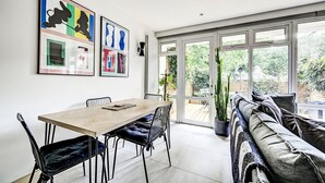 Un comedor con mesa y sillas de madera, un sofá con cojines y un ventanal con vistas a zonas verdes.