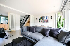 Ein modernes Wohnzimmer mit einem grauen Ecksofa, einem schwarzen Couchtisch und einer Treppe, die zu einer oberen Etage führt.