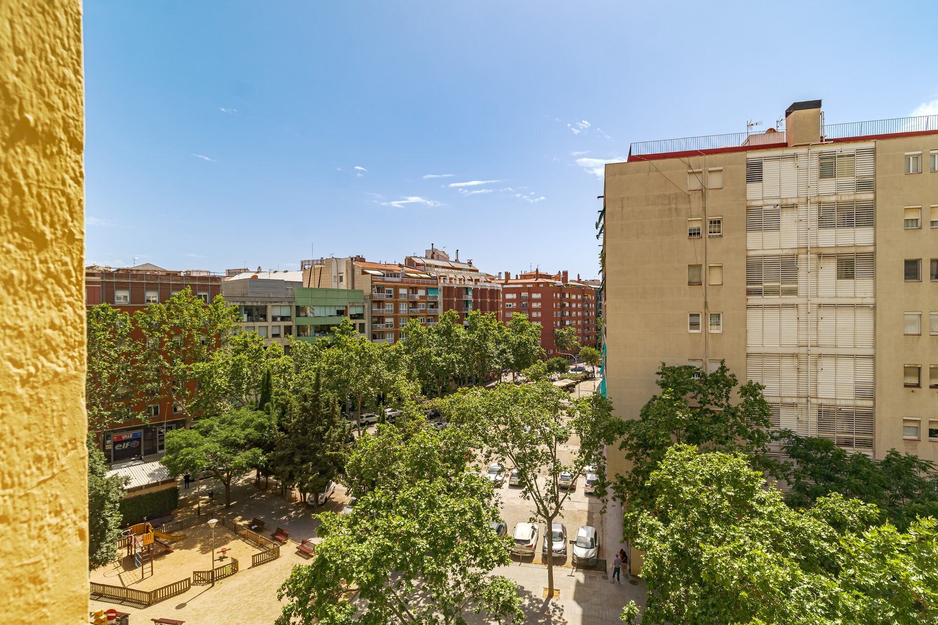 Um bairro residencial com edifícios altos, um parquinho e carros estacionados.