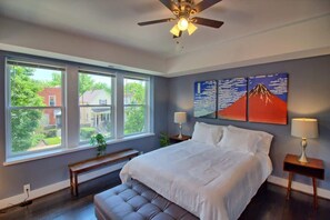 Une chambre avec un grand lit, deux lampes de chevet, un ventilateur de plafond et une fenêtre avec un banc.