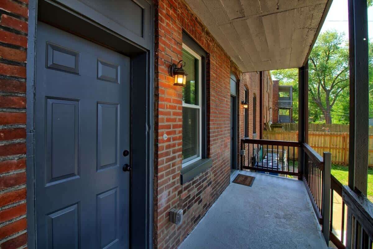A brick building with a grey door, a small porch, and a wooden fence in the background.