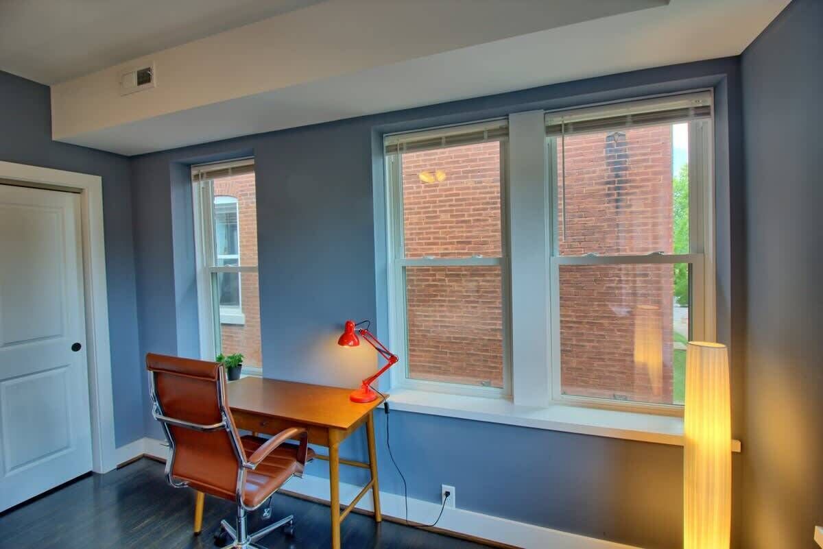 A room with a desk, chair, and two windows with blinds.