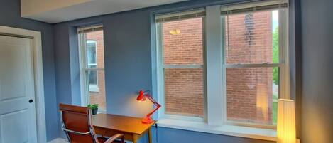 A room with a desk, chair, and two windows with blinds.