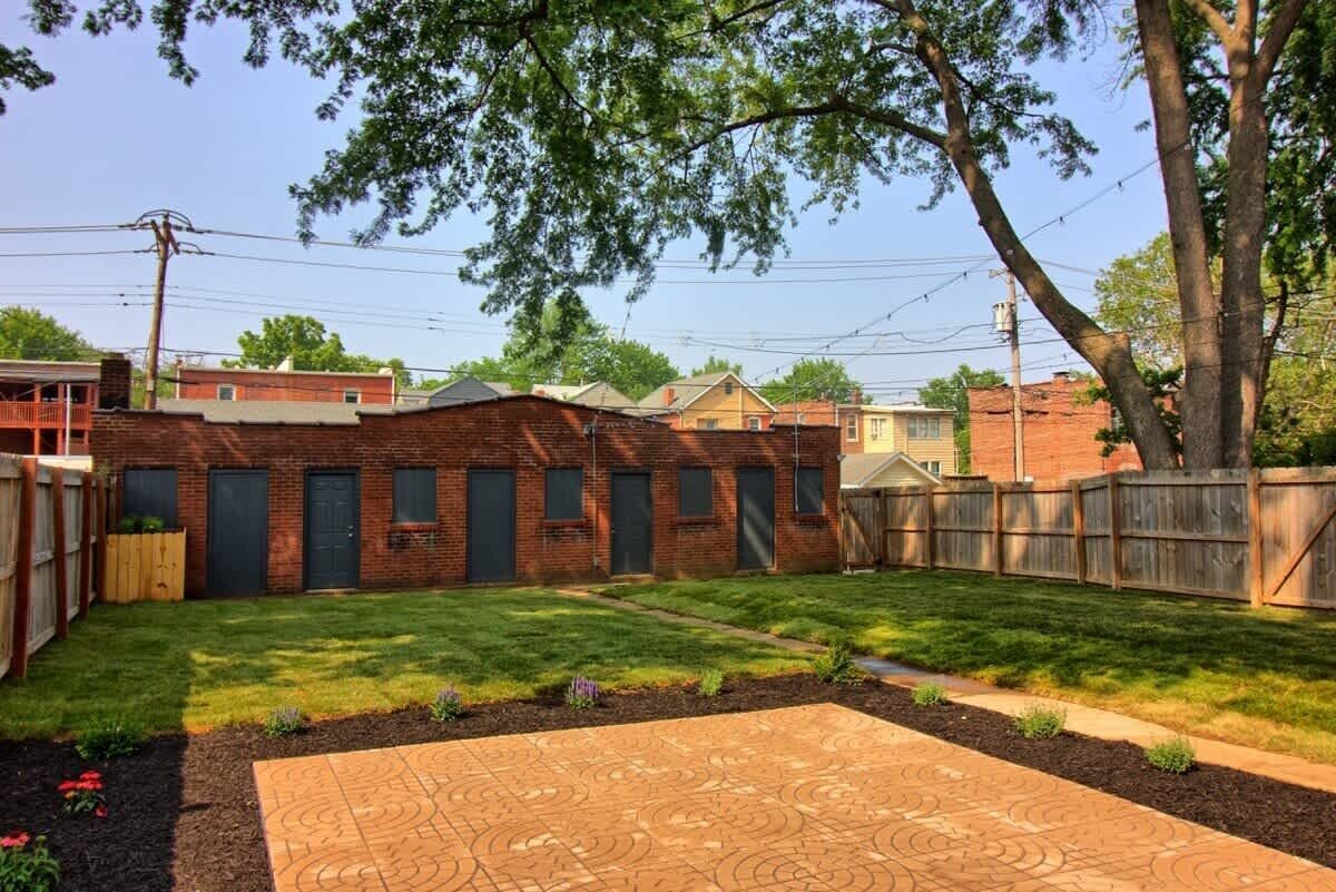 A backyard with a brick building, a wooden fence, and a paved patio area.