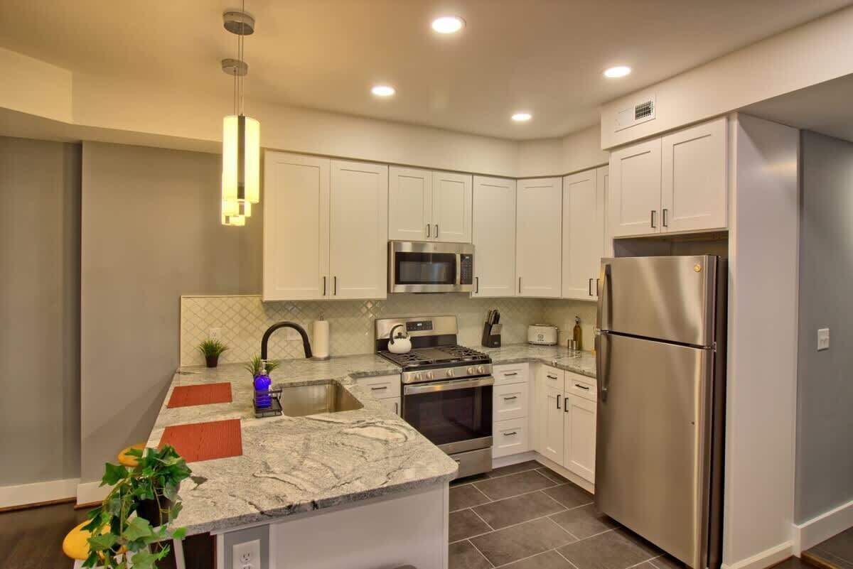 A modern kitchen with white cabinets, stainless steel appliances, and a marble countertop.