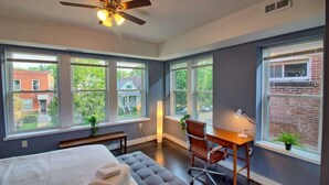 Ein Schlafzimmer mit einem Bett, einem Schreibtisch, einem Stuhl und großen Fenstern.