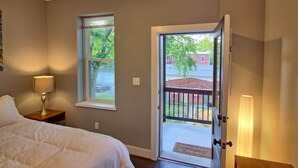 Ein Schlafzimmer mit Bett, Nachttisch, Lampe, Fenster und einer Tür, die nach draußen führt.