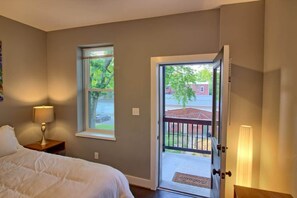 Une chambre à coucher avec un lit, une table de chevet, une lampe, une fenêtre et une porte donnant sur l’extérieur.