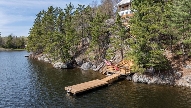 A lakeside property with a wooden dock, a wooden staircase leading to a house, and surrounding pine trees.