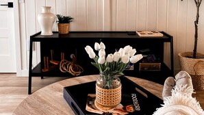 A living room with a black console table, a TV mounted on the wall, a plant, and a tray with a vase of flowers.