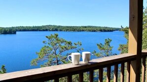 A wooden deck with two white mugs, overlooking a large body of water and a forested shoreline.