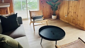 A wooden-floored living room with a sofa, a chair, a round table, and a potted plant.