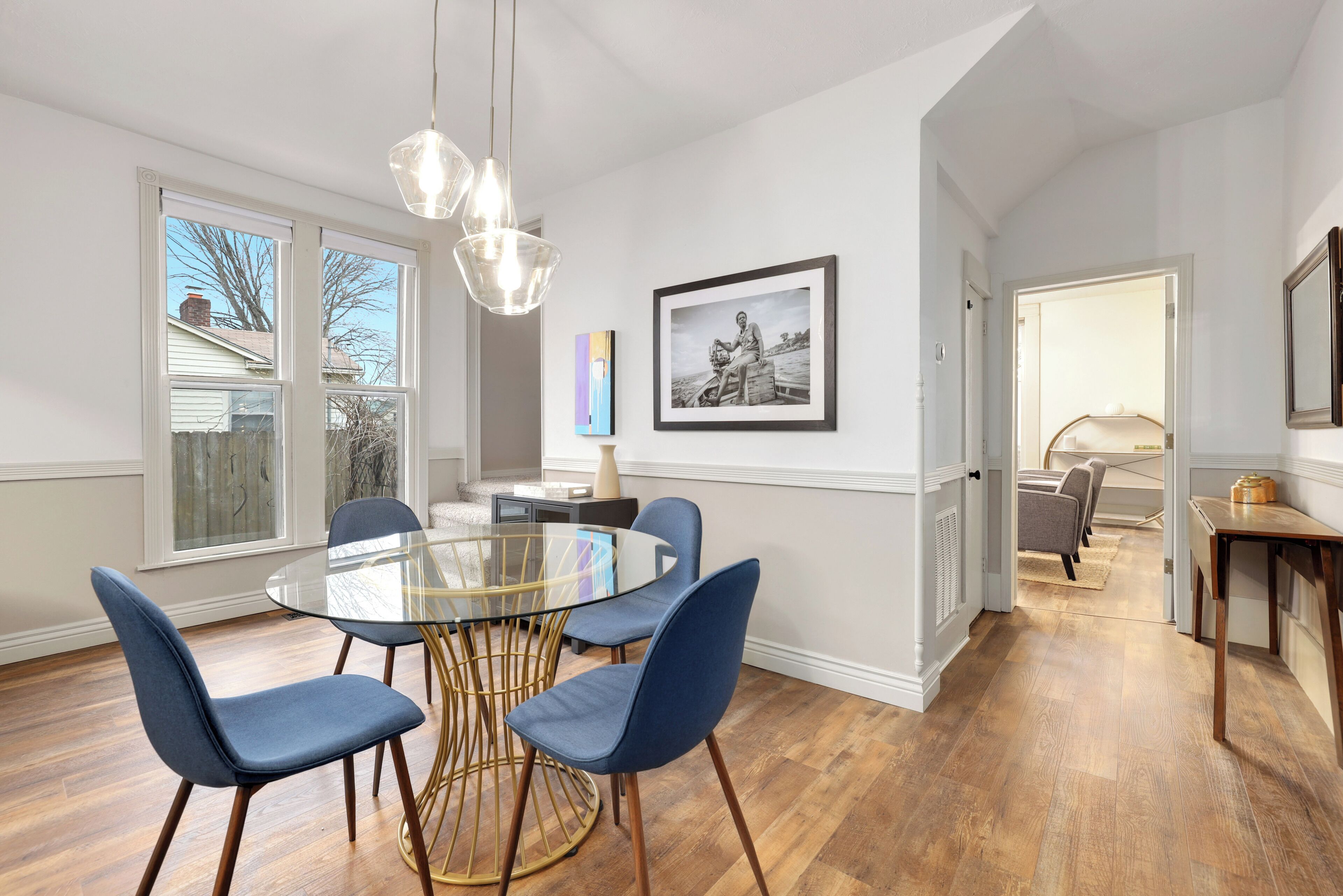 Un coin repas avec une table en verre, des chaises bleues et un luminaire suspendu.