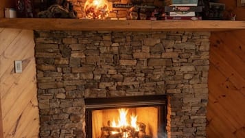 A stone fireplace with a fire, a shelf above with books and decorative items, and a cozy blanket on the floor.