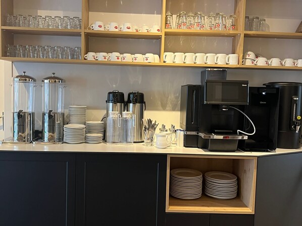 Una estación de café con una máquina de café, tazas y dispensador de agua.