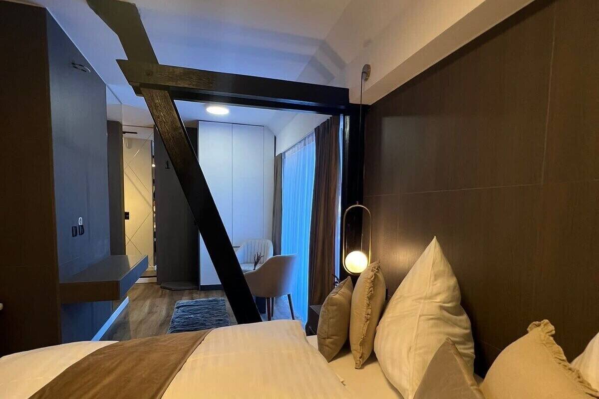 Hotellihuoneessa on suuri sänky, työpöytä ja tuoli. Taustalla näkyy toinen huone.