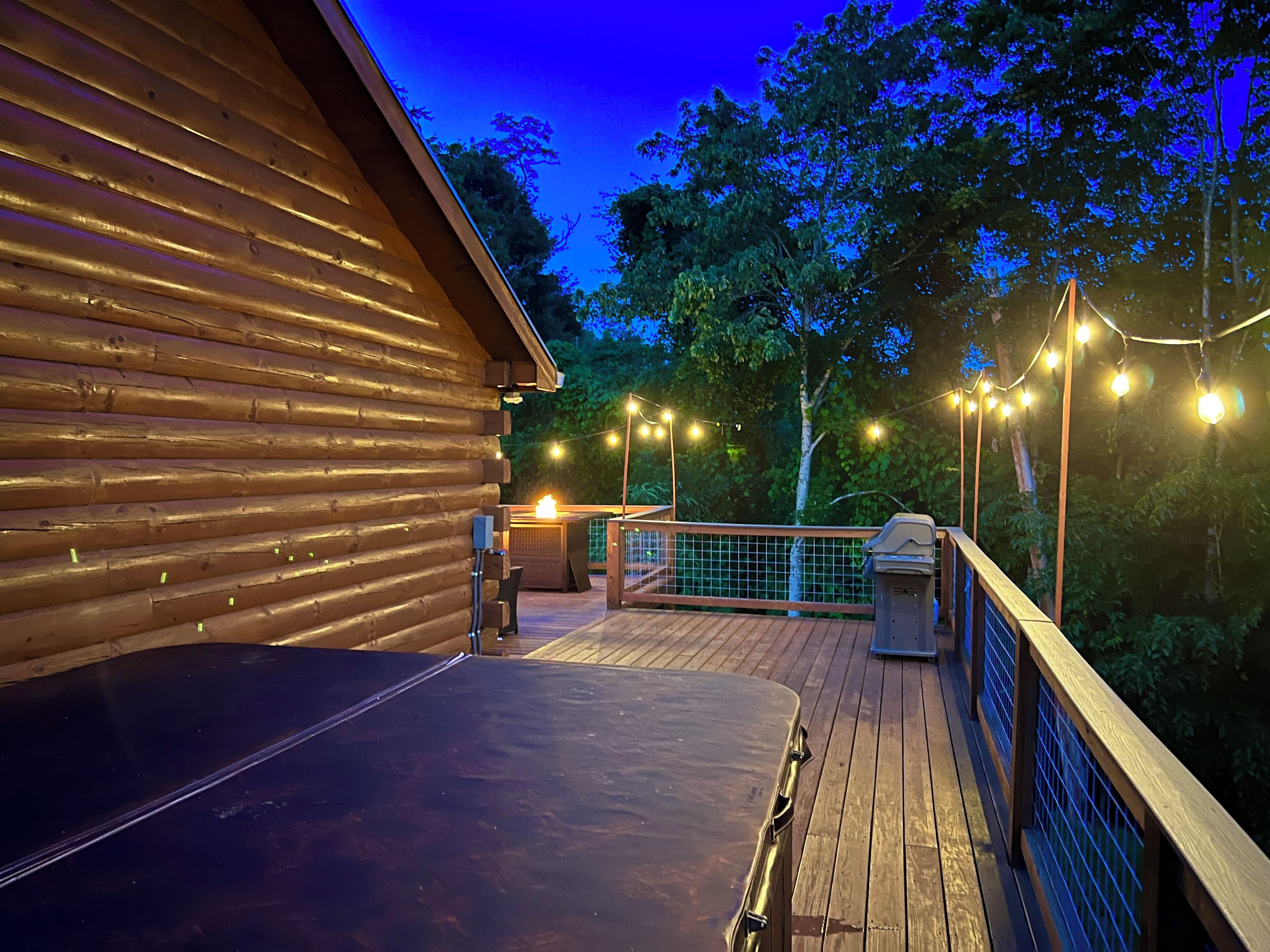 Un patio in legno con ringhiera in metallo, zona barbecue e luci decorative.