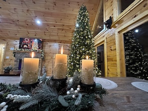 A cozy room with a wooden interior, a decorated Christmas tree, and three lit candles on a table.