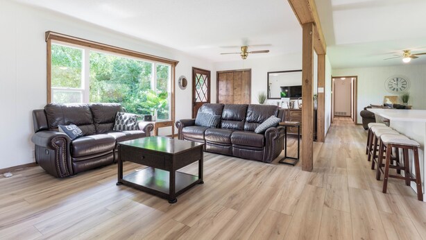 Un amplio salón con sofás de cuero, una mesa de centro de vidrio y piso de madera.