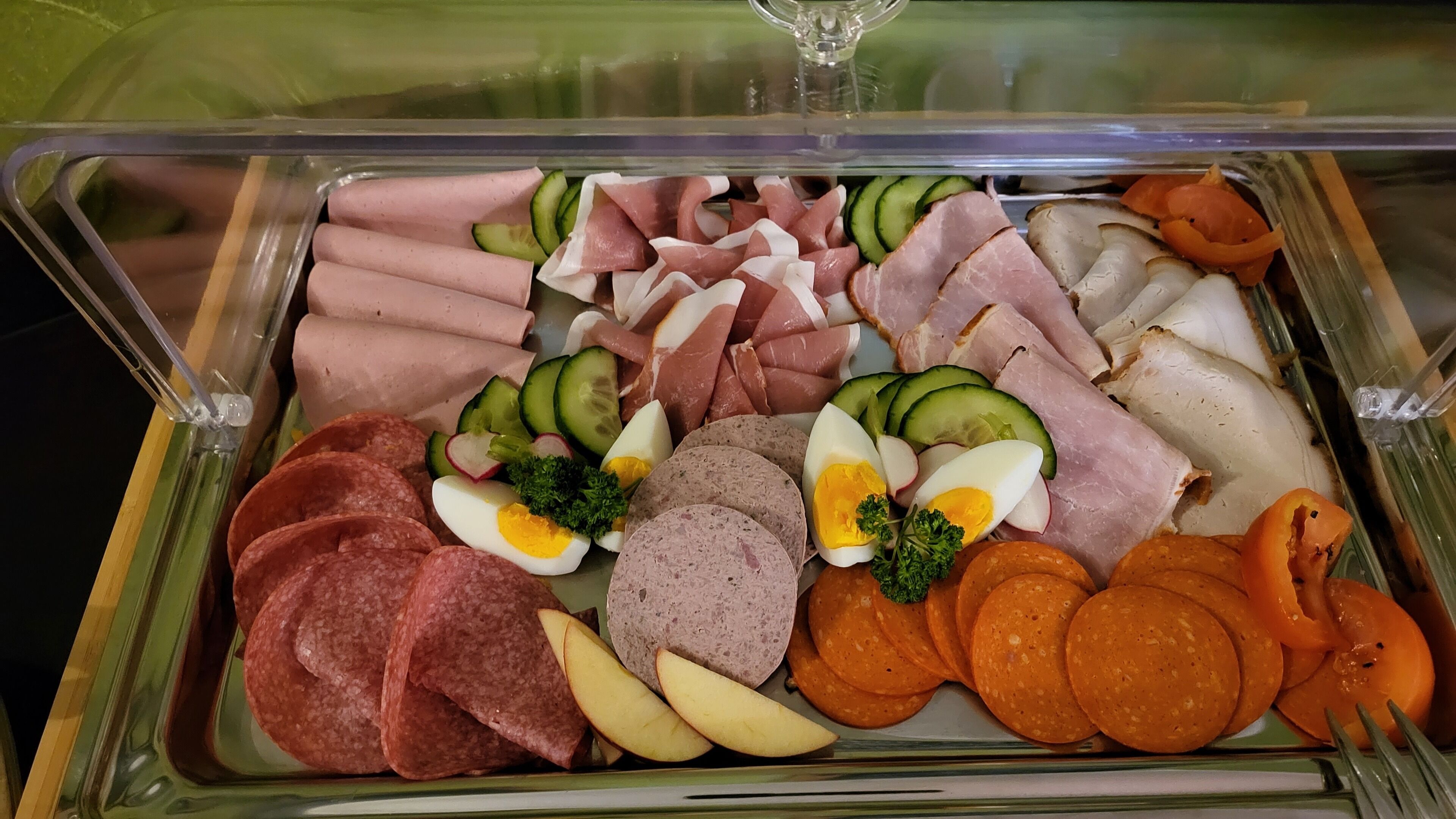 A glass display case containing various deli items including sliced meats, cheeses, and vegetables.