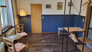 A room with a wooden door, a small table with a chair, a standing lamp, and a blue accent wall. - Pension Zur Neuenburg (Freyburg)