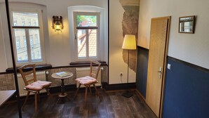 A cozy room with a wooden table and two chairs, a lamp, and a view of buildings through the windows. - Pension Zur Neuenburg (Freyburg)