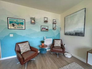 Uma sala de estar com duas poltronas de couro marrom, uma mesinha redonda com uma planta e um quadro pendurado.